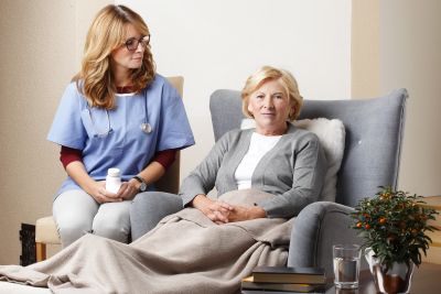 smiling home caregiver sitting with senior patient at living room